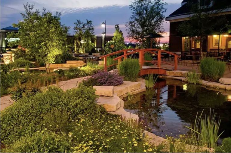 Twilight over a tranquil garden with a red bridge crossing a pond.